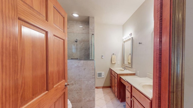 bathroom with a tile shower, vanity, and tile patterned flooring