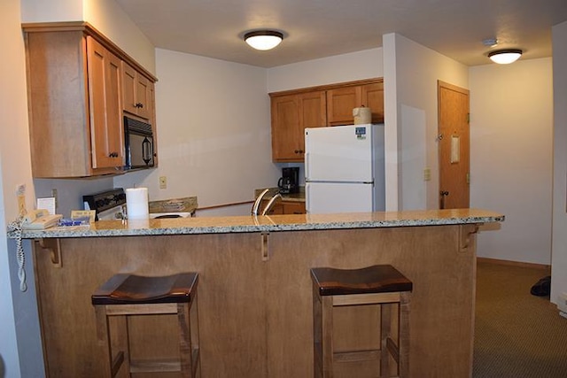 kitchen with kitchen peninsula, light stone counters, and white appliances