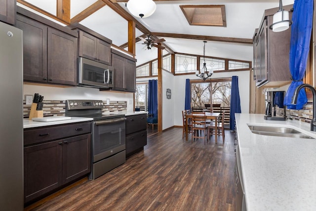 kitchen with appliances with stainless steel finishes, beamed ceiling, dark wood-type flooring, sink, and decorative light fixtures