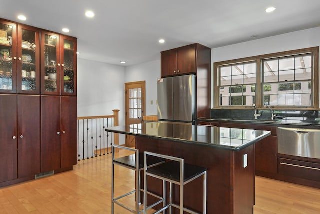 kitchen featuring a kitchen island, light wood-type flooring, stainless steel fridge, sink, and a kitchen bar