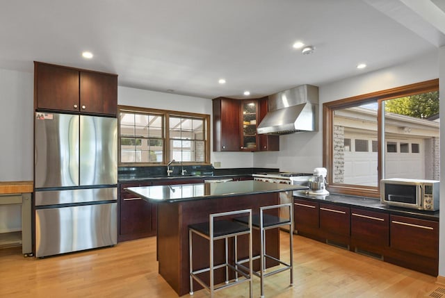 kitchen featuring a kitchen island, stainless steel appliances, wall chimney exhaust hood, sink, and light hardwood / wood-style floors