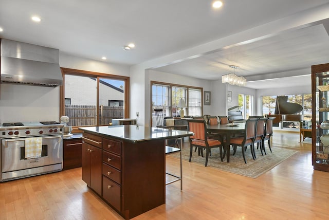 kitchen featuring decorative light fixtures, light hardwood / wood-style flooring, wall chimney range hood, designer range, and a center island