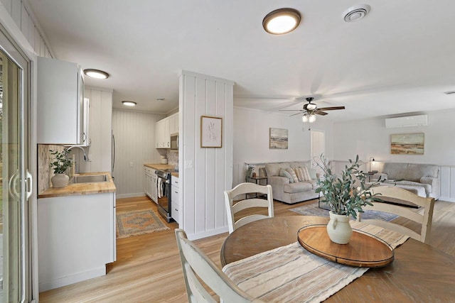 dining area with light hardwood / wood-style flooring, an AC wall unit, sink, and ceiling fan