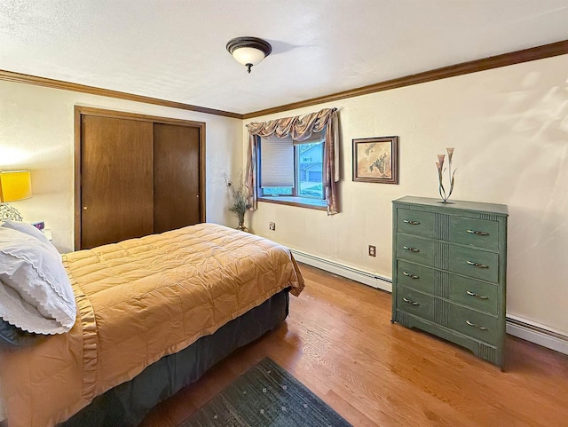 bedroom featuring baseboard heating, ornamental molding, hardwood / wood-style floors, and a closet