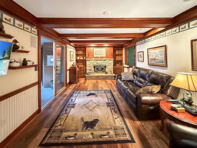 living room with beam ceiling, hardwood / wood-style flooring, built in features, and a stone fireplace