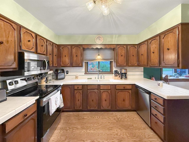 kitchen with kitchen peninsula, tasteful backsplash, appliances with stainless steel finishes, light wood-type flooring, and sink