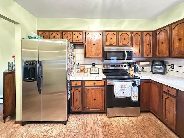 kitchen featuring light hardwood / wood-style floors, stainless steel appliances, tile countertops, and backsplash