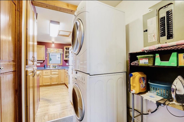 laundry room with light hardwood / wood-style flooring, stacked washer and dryer, and sink