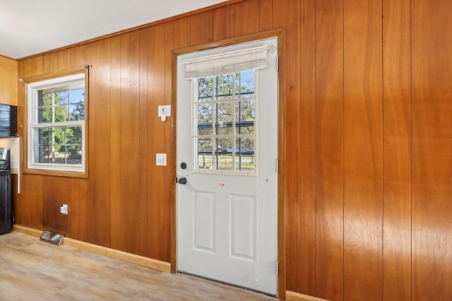 doorway to outside featuring light wood-type flooring, a healthy amount of sunlight, and wood walls