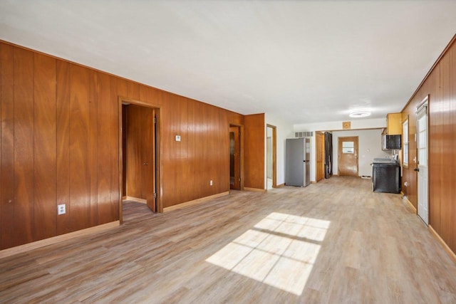 unfurnished living room featuring wooden walls and light hardwood / wood-style floors