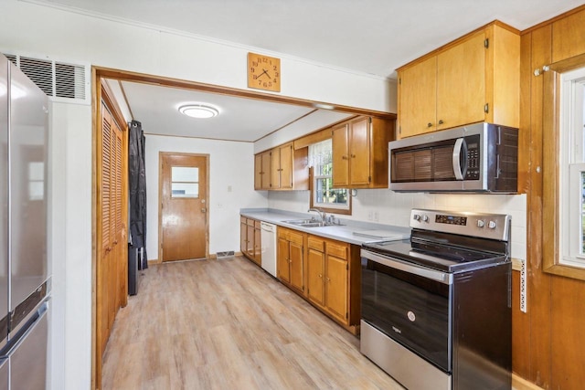 kitchen with appliances with stainless steel finishes, decorative backsplash, sink, and light wood-type flooring