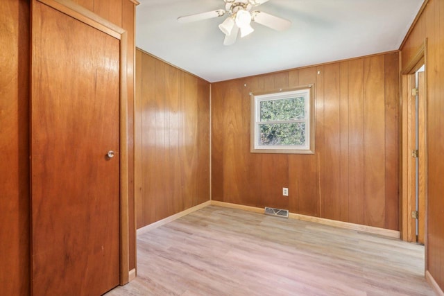 unfurnished room featuring ceiling fan, light hardwood / wood-style flooring, and wooden walls