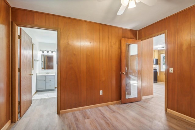 empty room featuring sink, wooden walls, light wood-type flooring, and ceiling fan