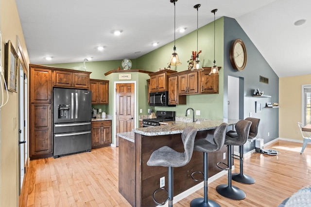 kitchen featuring lofted ceiling, light hardwood / wood-style flooring, black appliances, light stone countertops, and pendant lighting