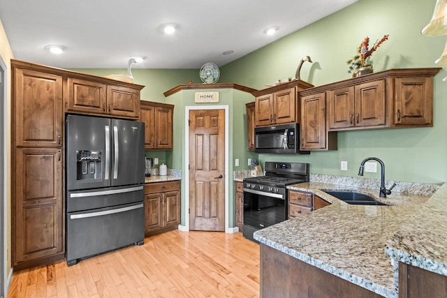 kitchen featuring light hardwood / wood-style floors, black appliances, sink, and light stone counters