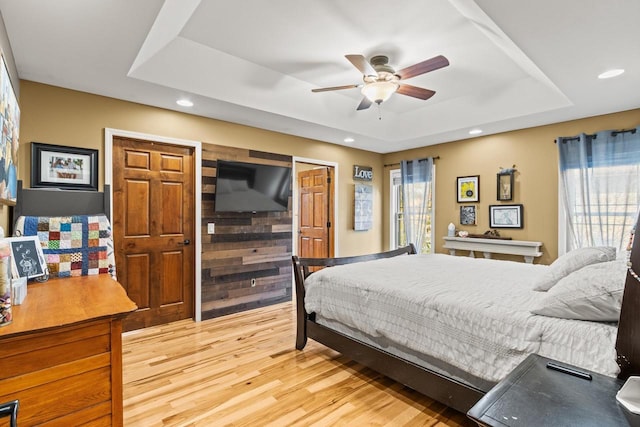 bedroom with ceiling fan, a raised ceiling, light wood-type flooring, and wooden walls