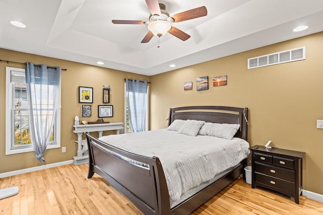 bedroom with light hardwood / wood-style flooring, a raised ceiling, and ceiling fan