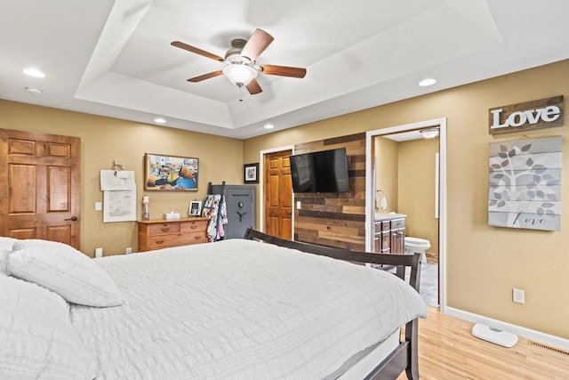 bedroom featuring a raised ceiling, hardwood / wood-style flooring, ensuite bathroom, and ceiling fan