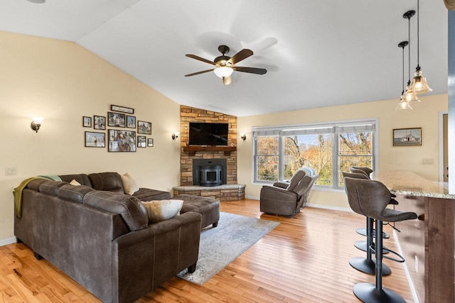 living room featuring vaulted ceiling, a wood stove, light hardwood / wood-style flooring, and ceiling fan