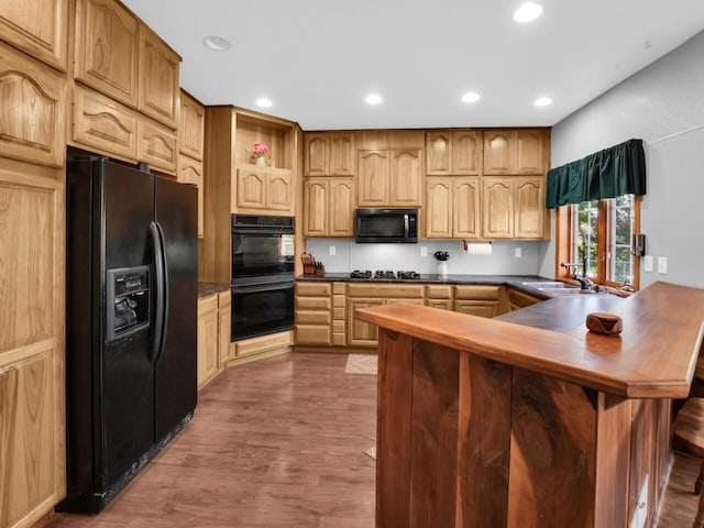 kitchen with black appliances, dark wood-type flooring, kitchen peninsula, and sink