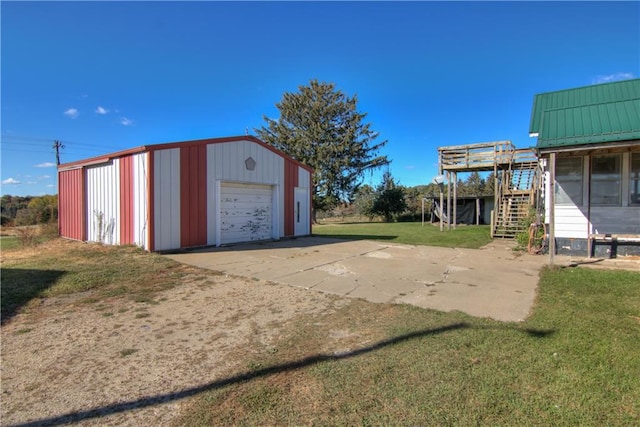 view of yard with a garage, concrete driveway, stairway, and an outbuilding