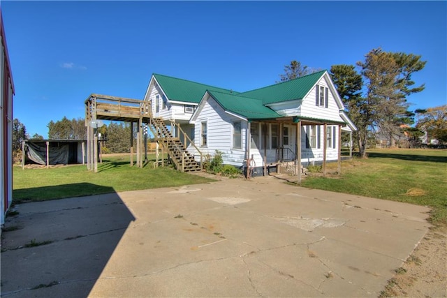 back of house with covered porch, stairs, metal roof, and a lawn