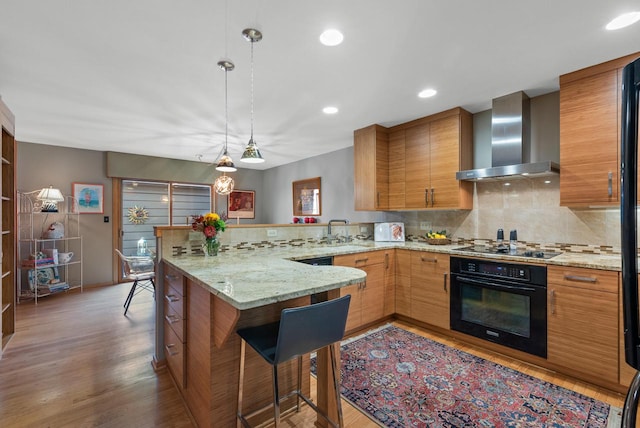 kitchen featuring wall chimney exhaust hood, kitchen peninsula, black appliances, a breakfast bar, and dark hardwood / wood-style flooring