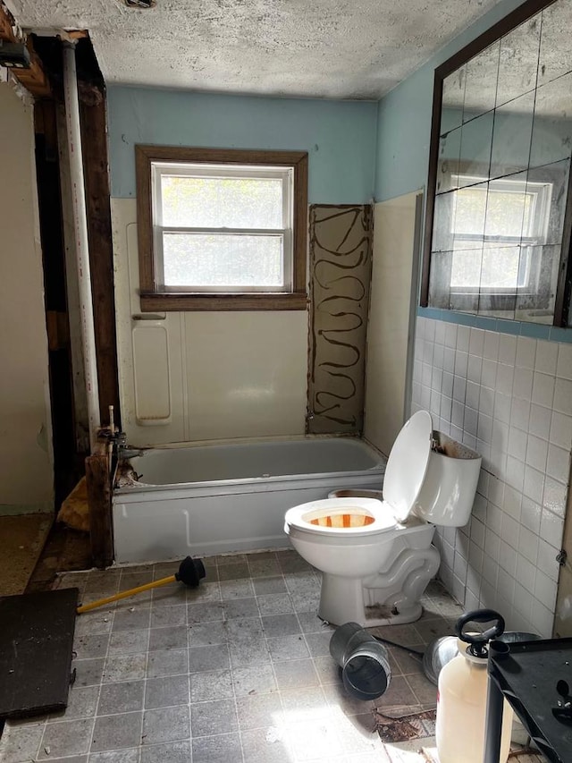 bathroom featuring toilet, a tub, a textured ceiling, and tile walls