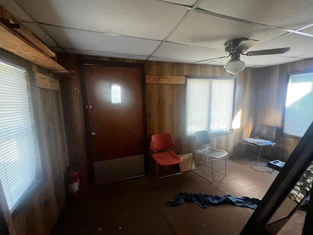 sitting room with ceiling fan, wood walls, and a drop ceiling