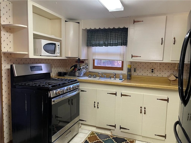 kitchen featuring white cabinets, light tile patterned floors, fridge, stainless steel range with gas stovetop, and sink