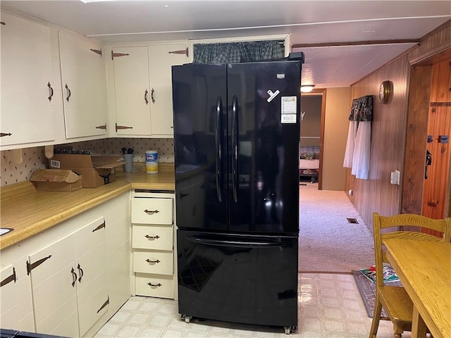 kitchen with white cabinets, backsplash, light colored carpet, and black refrigerator