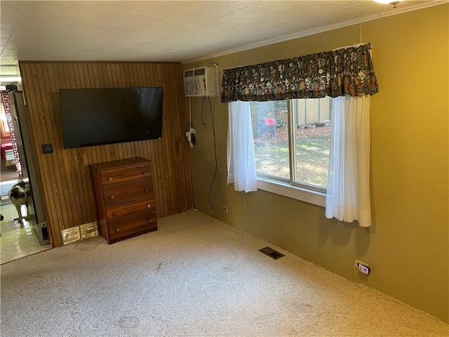 unfurnished living room featuring a wall mounted AC, ornamental molding, carpet flooring, a textured ceiling, and wood walls