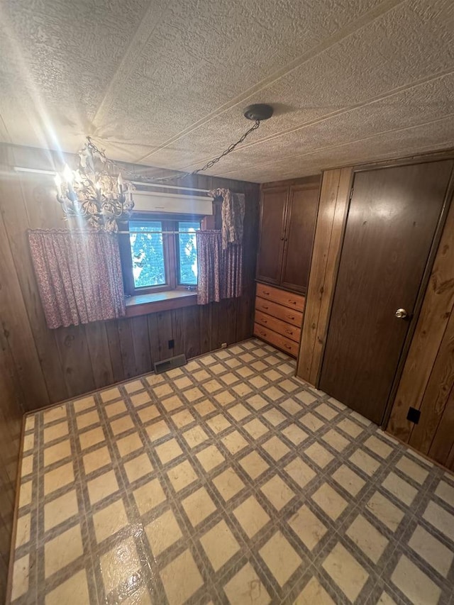 unfurnished room featuring wooden walls, a notable chandelier, and a textured ceiling