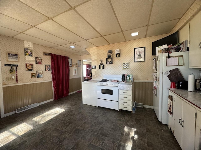 kitchen with a paneled ceiling, white cabinets, wooden walls, and white range oven