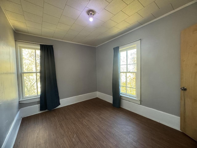 empty room with dark wood-type flooring, crown molding, and a healthy amount of sunlight