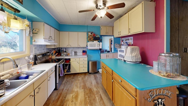 kitchen featuring stainless steel range with electric stovetop, sink, decorative light fixtures, light wood-type flooring, and ceiling fan