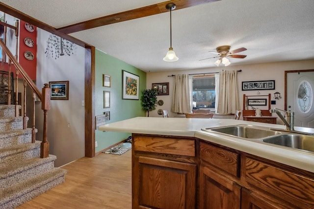 kitchen featuring ceiling fan, a textured ceiling, light wood-type flooring, sink, and decorative light fixtures