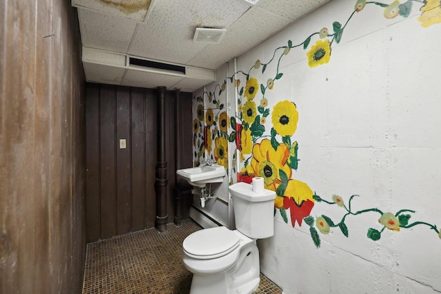 bathroom with a paneled ceiling, toilet, and wood walls