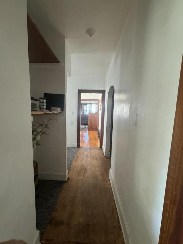 hallway with arched walkways, wood finished floors, and baseboards