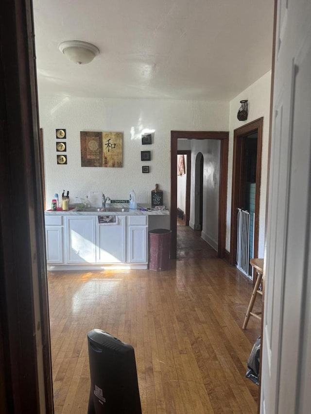 interior space featuring a sink, arched walkways, hardwood / wood-style flooring, white cabinetry, and light countertops
