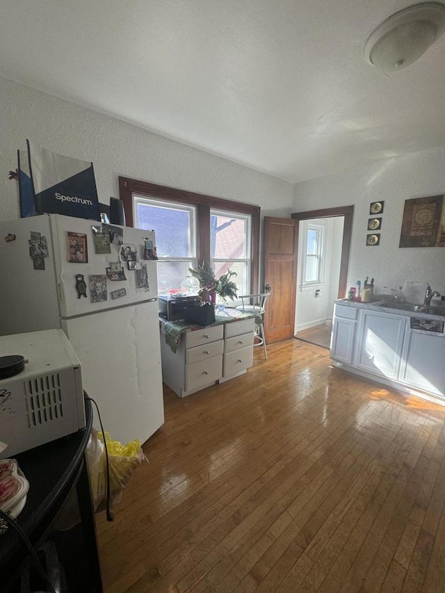 kitchen with white cabinets, a textured wall, light wood-type flooring, and freestanding refrigerator