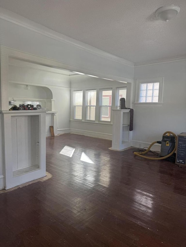 unfurnished living room with dark wood-type flooring, a textured ceiling, crown molding, and baseboards