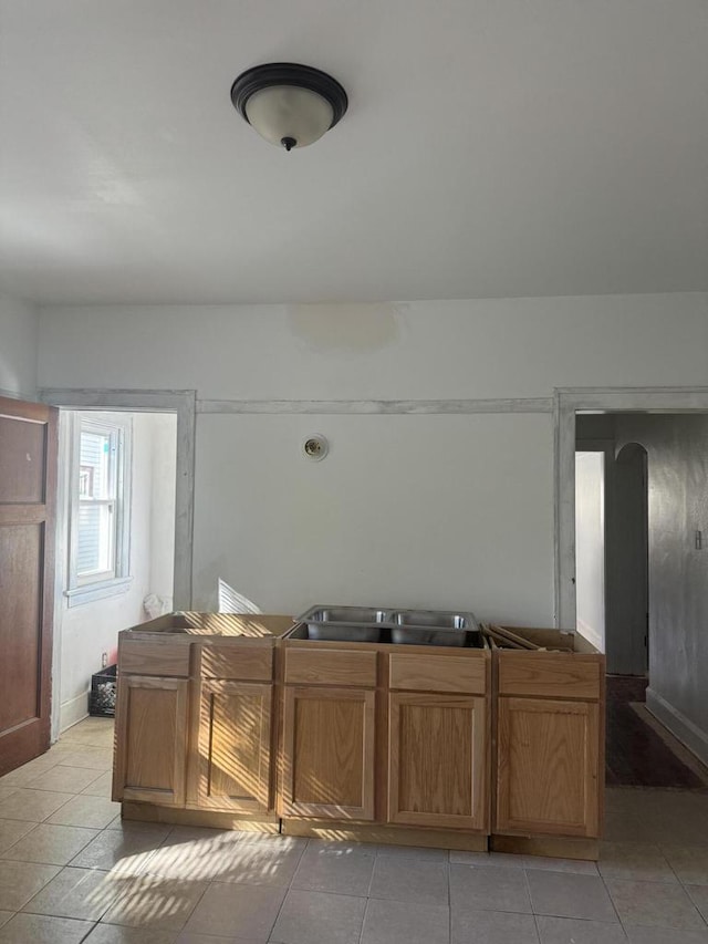 kitchen with brown cabinets, arched walkways, a sink, and light tile patterned floors