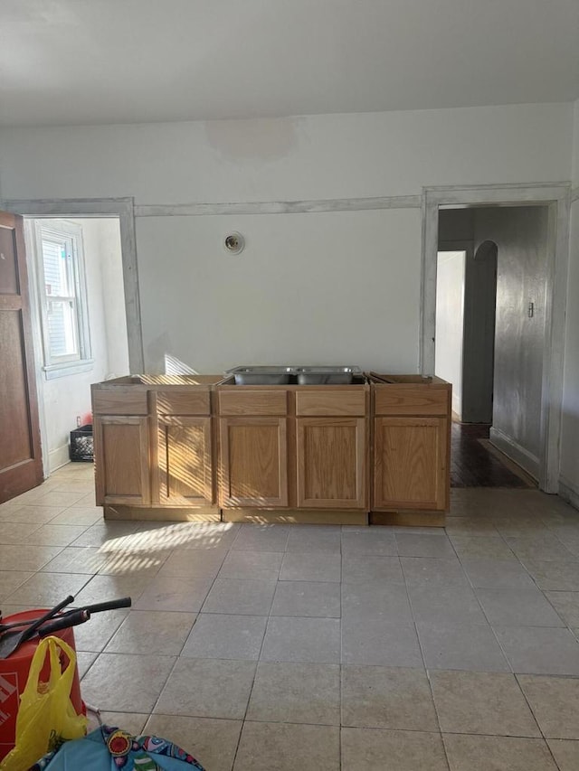 kitchen featuring arched walkways, brown cabinetry, a sink, and light tile patterned floors