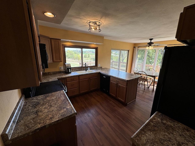 kitchen with dark wood-type flooring, kitchen peninsula, sink, black appliances, and a textured ceiling