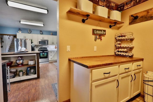 kitchen featuring white cabinets, appliances with stainless steel finishes, wood-type flooring, and wooden counters