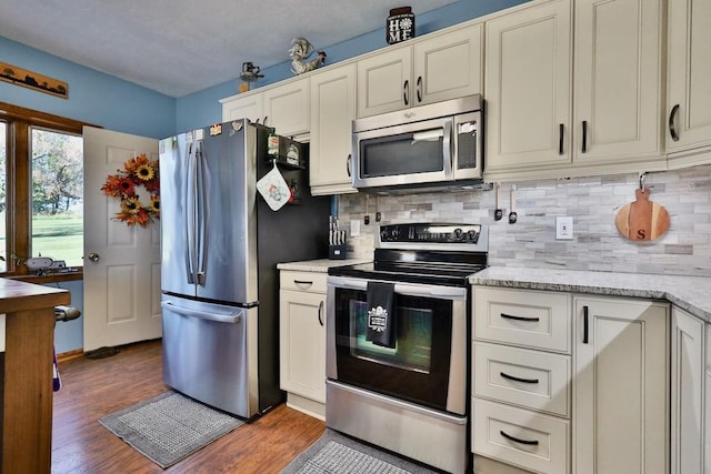 kitchen featuring light stone countertops, stainless steel appliances, dark wood-type flooring, and backsplash