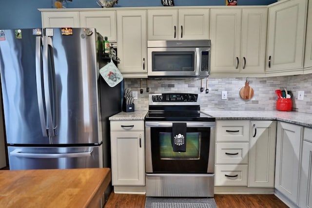 kitchen with tasteful backsplash, appliances with stainless steel finishes, dark hardwood / wood-style flooring, white cabinetry, and light stone counters