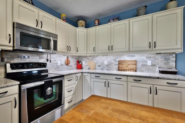 kitchen featuring white cabinetry, tasteful backsplash, stainless steel appliances, and light stone counters