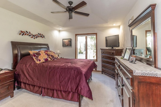 bedroom with light colored carpet, a raised ceiling, and ceiling fan